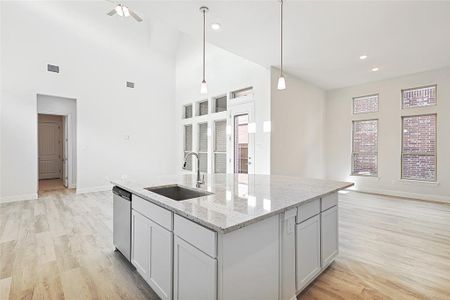 Kitchen featuring light stone countertops, sink, dishwasher, decorative light fixtures, and a center island with sink