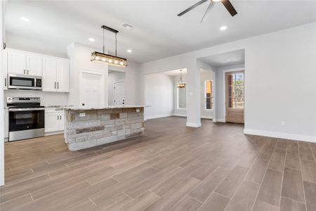 Kitchen with a center island, pendant lighting, stainless steel appliances, light stone countertops, and white cabinets