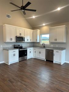 Kitchen with white cabinetry, sink, dishwashing machine, stove, and light stone countertops