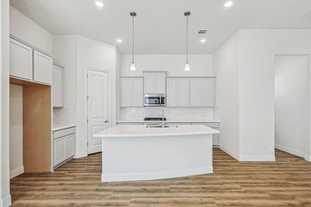 Kitchen featuring light wood-type flooring, a kitchen island with sink, and tasteful backsplash