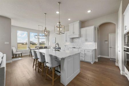 Kitchen featuring light stone countertops, backsplash, a kitchen island with sink, sink, and white cabinetry