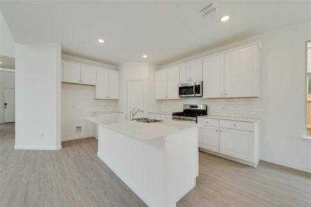 Kitchen with a kitchen island with sink, sink, white cabinets, and appliances with stainless steel finishes