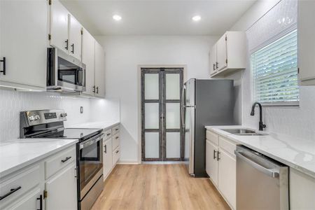 Kitchen featuring white cabinets, stainless steel appliances, light stone counters, and sink