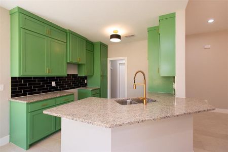 Kitchen with light stone counters, sink, kitchen peninsula, and green cabinets