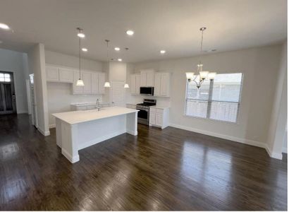 Kitchen with an quartz countertops on  island with sink, stainless steel appliances, white cabinets, dark wood-type flooring, and hanging light fixtures