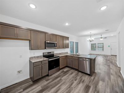 Kitchen featuring kitchen peninsula, hardwood / wood-style floors, decorative light fixtures, appliances with stainless steel finishes, and ceiling fan with notable chandelier