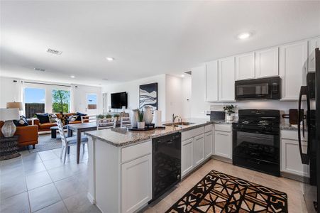 Kitchen with black appliances, sink, kitchen peninsula, light stone counters, and white cabinetry