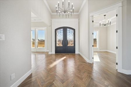 Entrance foyer with french doors, parquet flooring, an inviting chandelier, crown molding, and a towering ceiling