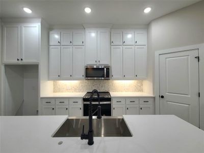 Kitchen featuring stainless steel appliances, sink, tasteful backsplash, and white cabinetry