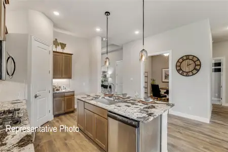 Kitchen with appliances with stainless steel finishes, light stone counters, light wood-type flooring, decorative light fixtures, and sink