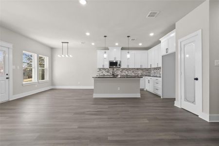 Kitchen with white cabinetry, hanging light fixtures, tasteful backsplash, and a center island with sink