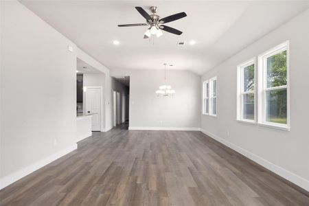 Spare room with ceiling fan with notable chandelier, dark wood-type flooring, and vaulted ceiling