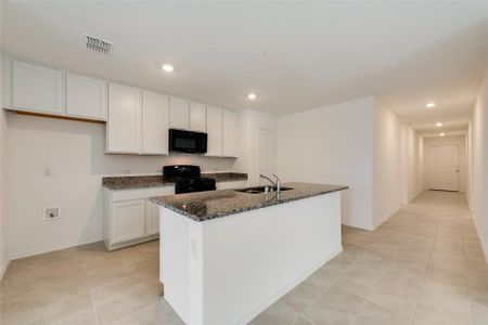 Kitchen featuring dark stone counters, black appliances, sink, white cabinetry, and a kitchen island with sink