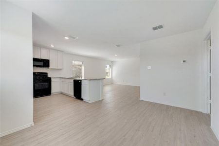 Kitchen featuring light stone countertops, white cabinets, black appliances, and light wood-type flooring