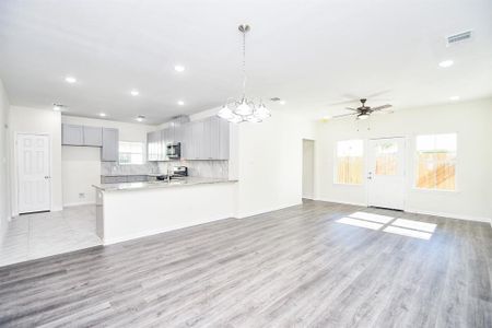 Bright, spacious kitchen and living area with modern appliances, gray cabinetry, wood flooring, pendant lighting, and double doors leading to a backyard.