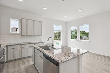 Kitchen featuring tasteful backsplash, stainless steel appliances, a center island with sink, sink, and light wood-type flooring