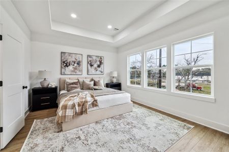 Spacious primary bedroom featuring large windows for abundant natural light, elegant tray ceiling, and a cozy atmosphere. Perfect for relaxation and comfort.