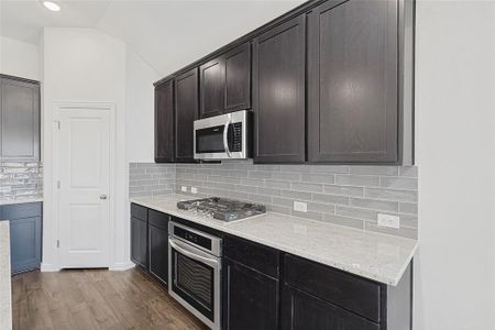 Kitchen with backsplash, stainless steel appliances, lofted ceiling, and wood-type flooring