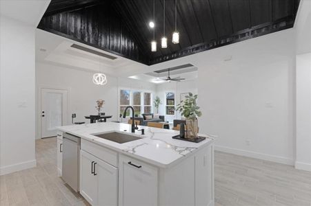 Kitchen with stainless steel dishwasher, white cabinets, a sink, an island with sink, and light stone countertops