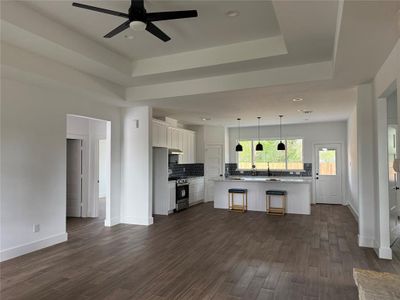 This is a spacious, modern open-plan living space with a well-equipped kitchen featuring white cabinetry and stainless steel appliances, accented by stylish pendant lights over the island. The area is finished with dark wood flooring and a contemporary ceiling fan, offering a comfortable and elegant setting for both living and entertaining.