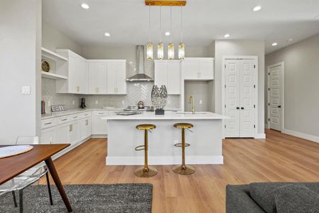 Kitchen with a kitchen island with sink, light countertops, a sink, and wall chimney exhaust hood