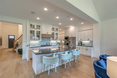 Kitchen with light hardwood / wood-style flooring, tasteful backsplash, a center island with sink, and stainless steel appliances