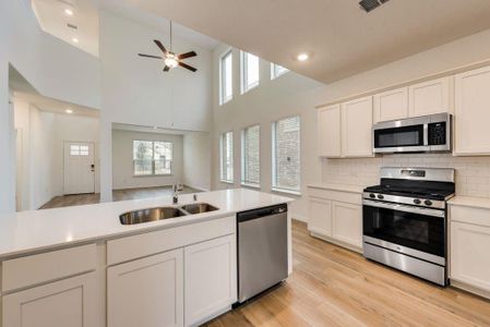 Kitchen featuring stainless steel appliances, sink, high vaulted ceiling, white cabinetry, and ceiling fan