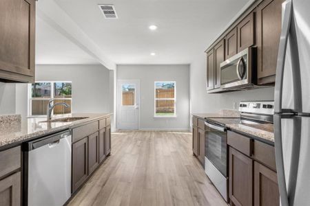 Kitchen with light hardwood / wood-style floors, light stone counters, a healthy amount of sunlight, and appliances with stainless steel finishes