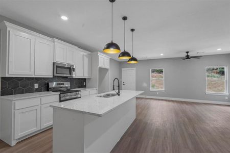 Kitchen with light stone counters, stainless steel appliances, white cabinetry, ceiling fan, and a kitchen island with sink