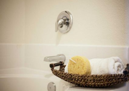 Driftwood stage model home bathroom with wicker tray that has yellow sponge and white towel in it sitting on the side of the bathtub