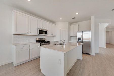 Kitchen featuring light hardwood / wood-style floors, sink, an island with sink, white cabinetry, and stainless steel appliances