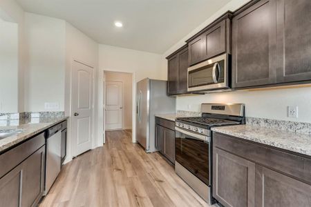 Kitchen with dark brown cabinets, light hardwood / wood-style floors, light stone countertops, and appliances with stainless steel finishes