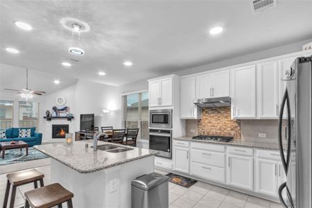 Kitchen featuring under cabinet range hood, white cabinets, open floor plan, appliances with stainless steel finishes, and a glass covered fireplace