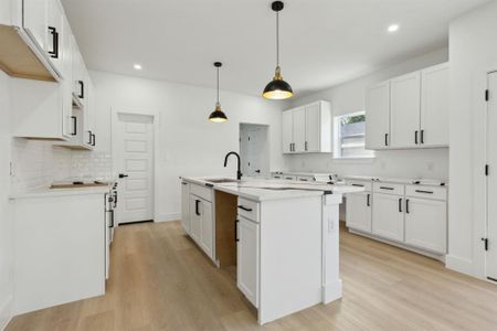 Kitchen with sink, an island with sink, decorative light fixtures, white cabinets, and light hardwood / wood-style flooring