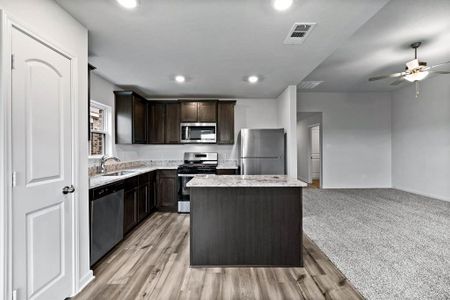 Kitchen with a center island, stainless steel appliances, dark brown cabinetry, ceiling fan, and light colored carpet