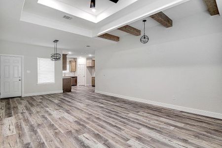 Unfurnished living room featuring beamed ceiling, wood-type flooring, and a raised ceiling