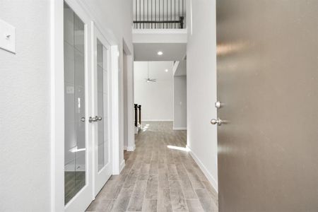 The grand entrance beckons with high ceilings, adorned with elegant wood-look tile flooring and oversized baseboards. Home office located in the forefront of the home. Sample photo of completed home with similar floor plan. As-built interior colors and selections may vary.