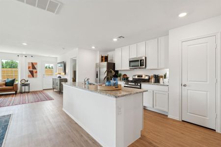 Kitchen with white cabinetry, a kitchen island with sink, light stone countertops, light wood-type flooring, and stainless steel appliances