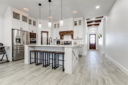 Kitchen featuring light countertops, appliances with stainless steel finishes, tasteful backsplash, an island with sink, and glass insert cabinets