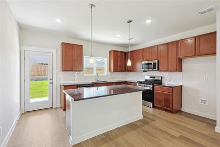 Kitchen featuring sink, a kitchen island, light hardwood / wood-style flooring, stainless steel appliances, and dark stone counters