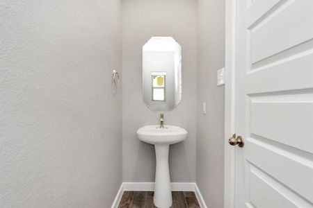 Experience modern elegance in this charming half bathroom, boasting a sophisticated 5-panel door, pedestal sink, contemporary hardware, and recessed lights. The warm paint palette bathes the area in a welcoming glow, creating a bright and inviting atmosphere. Sample photo of completed home with similar floor plan. As-built interior colors and selections may vary.