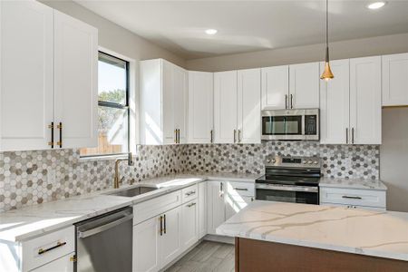 Kitchen featuring stainless steel appliances, pendant lighting, white cabinets, and sink