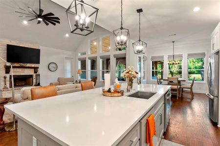 Kitchen with hanging light fixtures, sink, a stone fireplace, a center island with sink, and stainless steel appliances