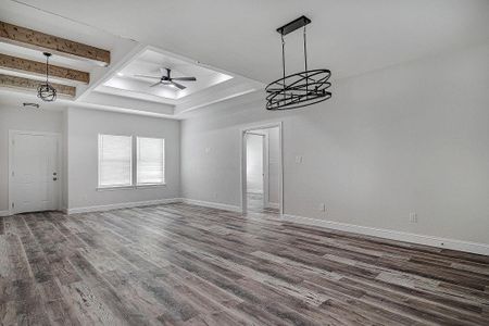 Unfurnished living room with ceiling fan with notable chandelier, beamed ceiling, and hardwood / wood-style flooring