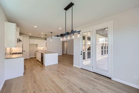 Kitchen featuring appliances with stainless steel finishes, light hardwood / wood-style floors, decorative light fixtures, white cabinets, and a kitchen island with sink