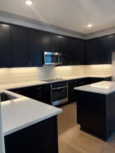 Kitchen with stainless steel appliances, backsplash, light wood-style floors, and dark cabinets