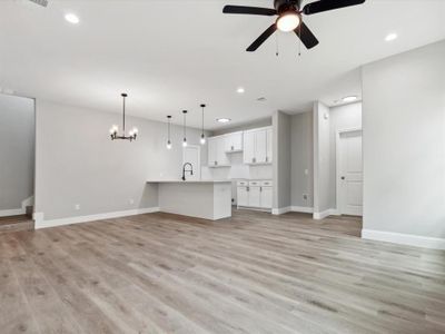 Unfurnished living room with sink, light wood-type flooring, and ceiling fan with notable chandelier