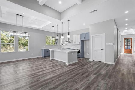 Kitchen with a center island with sink, tasteful backsplash, decorative light fixtures, dark wood-type flooring, and wall chimney range hood