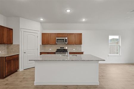 Kitchen featuring light hardwood / wood-style floors, stainless steel appliances, sink, and an island with sink