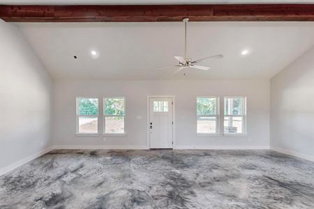 Empty room with a wealth of natural light, ceiling fan, and lofted ceiling with beams